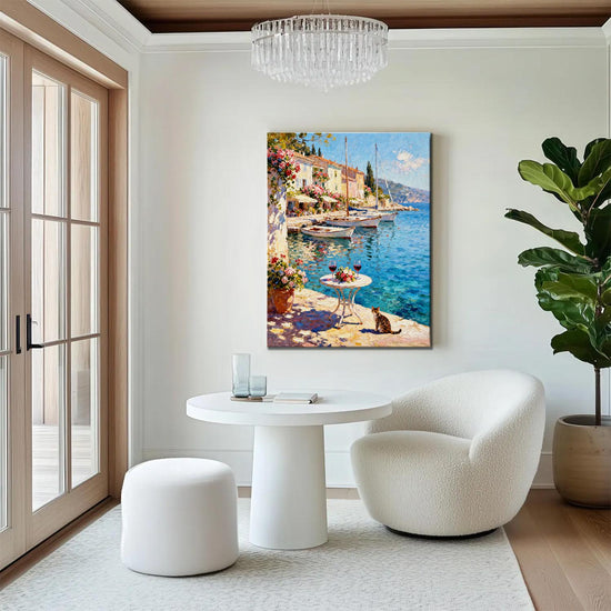 wall art canvas painting in the living room showing a sunny seaside town with a table of red wine and flowers on the pier and a cat.