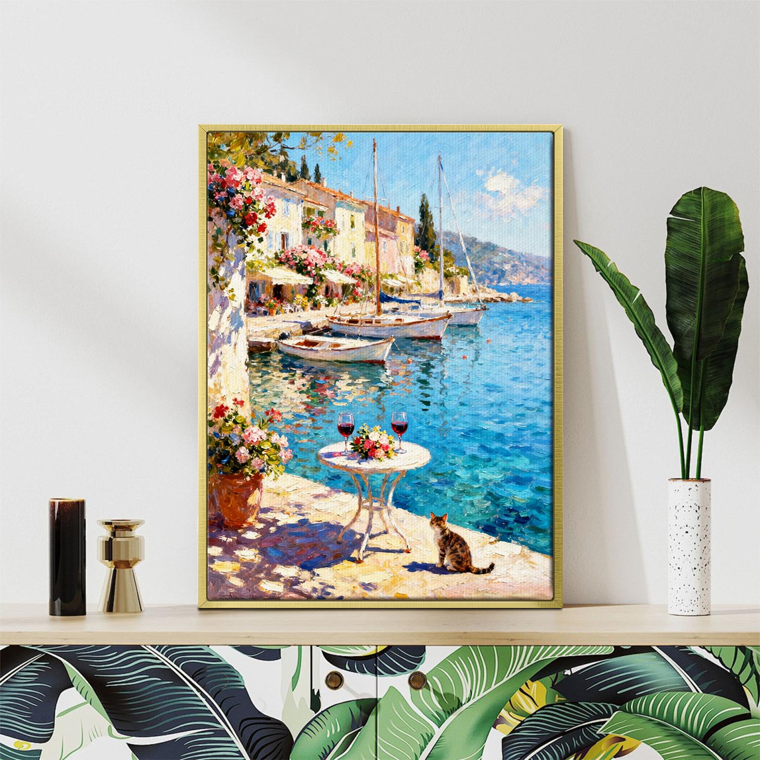 gold frame wall art canvas painting showing a sunny seaside town with a table of red wine and flowers on the pier and a cat.